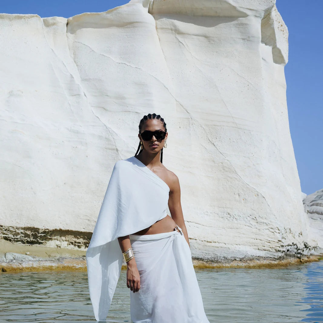 Γυναικείο μοντέλο φορά τα OS Sunglasses Formentera Petrolio καθισμένο σε λευκό βραχώδες τοπίο